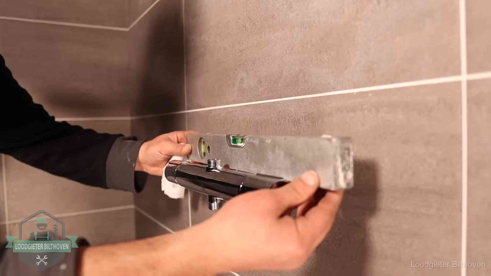 Loodgieter lijnt een douchekraan uit met een waterpas in een woning in Bilthoven