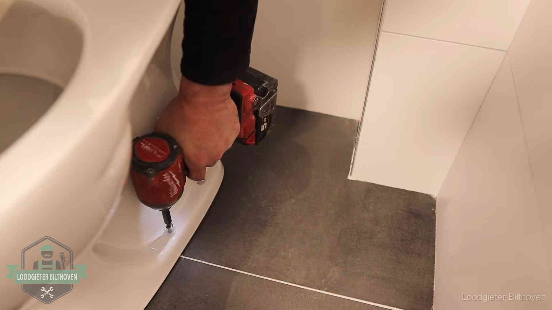 Loodgieter zet de voet van een wc-pot vast op de tegelvloer in Bilthoven